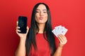 Young beautiful hispanic girl holding smartphone showing screen and poker cards looking at the camera blowing a kiss being lovely