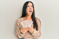 Young beautiful hispanic girl holding 10 united kingdom pounds banknotes angry and mad screaming frustrated and furious, shouting