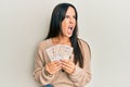 Young beautiful hispanic girl holding 10 united kingdom pounds banknotes angry and mad screaming frustrated and furious, shouting