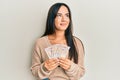 Young beautiful hispanic girl holding 10 united kingdom pounds banknotes smiling looking to the side and staring away thinking