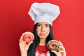 Young beautiful hispanic girl wearing chef hat holding homemade doughnut depressed and worry for distress, crying angry and afraid