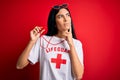 Young beautiful hispanic lifeguard woman wearing safeguard t-shirt holding whistle serious face thinking about question, very