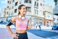 Young beautiful hispanic sport woman wearing runner outfit and headphones, drinking fresh water from the bottle Royalty Free Stock Photo