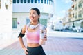 Young beautiful hispanic sport woman wearing runner outfit and headphones, drinking fresh water from the bottle Royalty Free Stock Photo