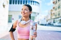 Young beautiful hispanic sport woman wearing runner outfit and headphones, drinking fresh water from the bottle Royalty Free Stock Photo