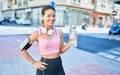 Young beautiful hispanic sport woman wearing runner outfit and headphones, drinking fresh water from the bottle Royalty Free Stock Photo