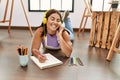 Young beautiful hispanic woman artist listening to music drawing on notebook at art studio Royalty Free Stock Photo