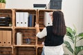 Young beautiful hispanic woman business worker holding documents of shelving at office Royalty Free Stock Photo