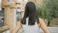 A young, beautiful hispanic woman caught in a casual, outdoor portrait, standing backward in a green city park, her back view