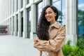 Young beautiful hispanic woman with curly hair outside office building, company worker smiling and looking at camera Royalty Free Stock Photo
