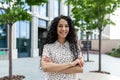 Young beautiful hispanic woman with curly hair smiling and looking at camera, businesswoman with arms crossed outside Royalty Free Stock Photo