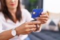 Young beautiful hispanic woman cutting credit card sitting on sofa at home Royalty Free Stock Photo