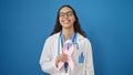 Young beautiful hispanic woman doctor holding breast cancer awareness pink ribbon over isolated blue background Royalty Free Stock Photo