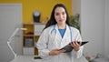 Young beautiful hispanic woman doctor holding clipboard smiling at the clinic Royalty Free Stock Photo