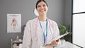 Young beautiful hispanic woman doctor smiling confident holding clipboard at clinic Royalty Free Stock Photo