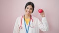 Young beautiful hispanic woman doctor smiling confident holding heart over isolated pink background Royalty Free Stock Photo