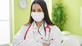 Young beautiful hispanic woman doctor standing with arms crossed gesture wearing medical mask at clinic Royalty Free Stock Photo