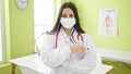 Young beautiful hispanic woman doctor standing with arms crossed gesture wearing medical mask at clinic Royalty Free Stock Photo