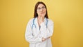 Young beautiful hispanic woman doctor standing with doubt expression thinking over isolated yellow background Royalty Free Stock Photo