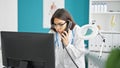 Young beautiful hispanic woman doctor using computer talking on telephone at clinic Royalty Free Stock Photo