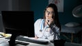 Young beautiful hispanic woman doctor using computer talking on telephone at clinic Royalty Free Stock Photo