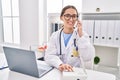 Young beautiful hispanic woman doctor using laptop talking on telephone at clinic Royalty Free Stock Photo