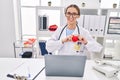 Young beautiful hispanic woman doctor using laptop working holding heart at clinic Royalty Free Stock Photo