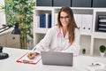 Young beautiful hispanic woman doctor using laptop writing on clipboard at clinic Royalty Free Stock Photo