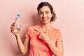 Young beautiful hispanic woman drinking bottle of water smiling happy pointing with hand and finger Royalty Free Stock Photo