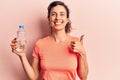 Young beautiful hispanic woman drinking bottle of water smiling happy and positive, thumb up doing excellent and approval sign Royalty Free Stock Photo