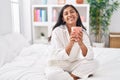 Young beautiful hispanic woman drinking cup of coffee sitting on bed at bedroom Royalty Free Stock Photo