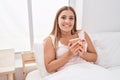 Young beautiful hispanic woman drinking cup of coffee sitting on bed at bedroom Royalty Free Stock Photo