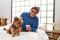 Young beautiful hispanic woman drinking cup of coffee sitting on bed with dog at bedroom Royalty Free Stock Photo