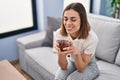 Young beautiful hispanic woman drinking tea sitting on sofa at home Royalty Free Stock Photo