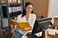 Young beautiful hispanic woman ecommerce business agent reading book at office