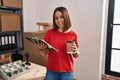 Young beautiful hispanic woman ecommerce business worker holding checklist drinking coffee at office Royalty Free Stock Photo