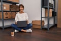 Young beautiful hispanic woman ecommerce business worker using laptop sitting on floor at office Royalty Free Stock Photo