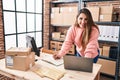 Young beautiful hispanic woman ecommerce business worker using laptop writing on notebook at office Royalty Free Stock Photo