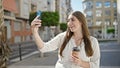 Young beautiful hispanic woman having video call drinking coffee at street Royalty Free Stock Photo