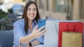 Young beautiful hispanic woman having video call sitting on table with shopping bags at coffee shop terrace Royalty Free Stock Photo