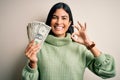 Young beautiful hispanic woman holding a pack of one dollar bunch of dollars doing ok sign with fingers, excellent symbol Royalty Free Stock Photo