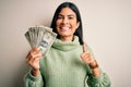 Young beautiful hispanic woman holding a pack of one dollar bunch of dollars happy with big smile doing ok sign, thumb up with Royalty Free Stock Photo