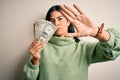 Young beautiful hispanic woman holding a pack of one dollar bunch of dollars with open hand doing stop sign with serious and Royalty Free Stock Photo