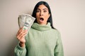 Young beautiful hispanic woman holding a pack of one dollar bunch of dollars scared in shock with a surprise face, afraid and Royalty Free Stock Photo