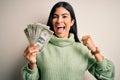 Young beautiful hispanic woman holding a pack of one dollar bunch of dollars screaming proud and celebrating victory and success Royalty Free Stock Photo