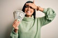 Young beautiful hispanic woman holding a pack of one dollar bunch of dollars stressed with hand on head, shocked with shame and Royalty Free Stock Photo