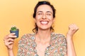 Young beautiful hispanic woman holding small cactus pot screaming proud, celebrating victory and success very excited with raised