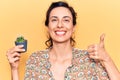 Young beautiful hispanic woman holding small cactus pot smiling happy and positive, thumb up doing excellent and approval sign Royalty Free Stock Photo