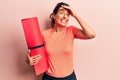 Young beautiful hispanic woman holding yoga mat stressed and frustrated with hand on head, surprised and angry face Royalty Free Stock Photo