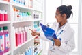 Young beautiful hispanic woman pharmacist organizing shelving at pharmacy